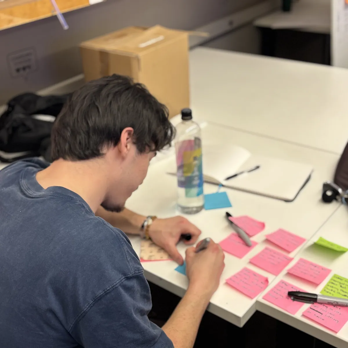 Jayden writing on sticky notes at a desk, planning Strata